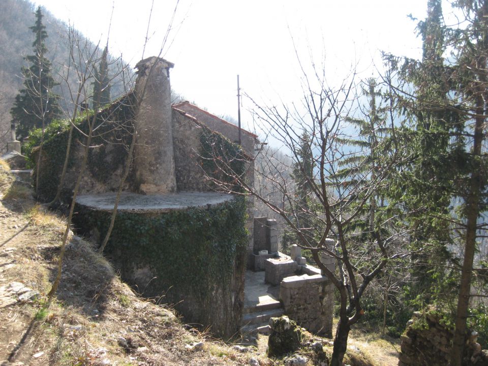 stara hiška z zunanjim dimnikom in majhno teraso, prislonjena ob pobočje